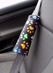 Seat belt pad with Multi-coloured paw prints on a black background handmade from fleece fabric